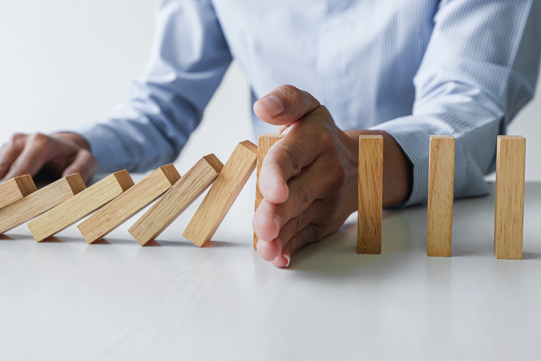 wooden dominos falling with a hand stopping the motion halfway